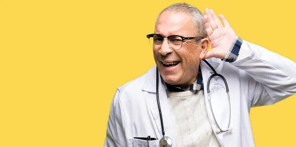 英俊的资深医生穿着医疗外套微笑着用手在耳朵听一个谣言或流言蜚语 耳聋概念 — 图库照片