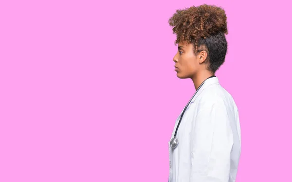 Young african american doctor woman over isolated background looking to side, relax profile pose with natural face with confident smile.