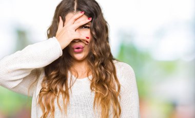 Mahcup ifadeyle parmaklarımın arasından seyir yüz ve gözler el ile kapsayan şok bakmak beyaz kazak giyen genç güzel kadın.