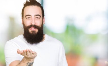 Uzun saç ve sakal bir öpücük el ile güzel ve seksi olmak hava üfleme kamera bakarak casual beyaz t-shirt giyen genç hipster adam. Aşk ifade.
