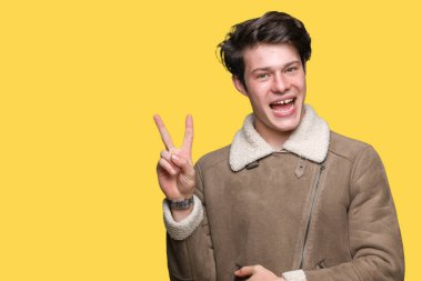 Mutlu yüz zafer işareti yaparken kameraya göz kırpıyor ile gülümseyen izole arka plan üzerinde kış ceket giyen genç yakışıklı adam. İki numaralı.