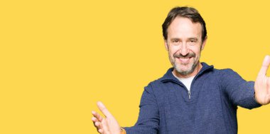 Orta yaş yakışıklı adam sarılmak için açık kollar ile gülümseyen kamera bakarak bir kazak giyiyor. Mutluluğu kucaklayan neşeli ifade.