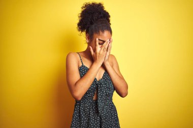 Ağlayan iken elleri ile yüz kapsayan üzücü ifade ile izole sarı arka plan üzerinde yaz Casual yeşil elbise giyen Afrikalı Amerikalı kadın. Depresyon konsepti.