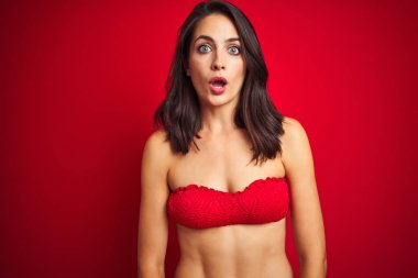 Kırmızı izole arka plan üzerinde bikini mayo giyen güzel kadın korkmuş ve sürpriz ifade ile şok, korku ve heyecanlı yüz.