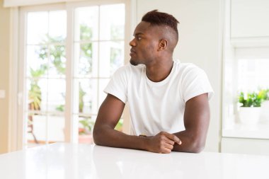 Yakışıklı afro-amerikan adam evde beyaz masada yan bakıyor, kendine güvenen gülümseme ile doğal yüzü ile profil poz dinlenmek.