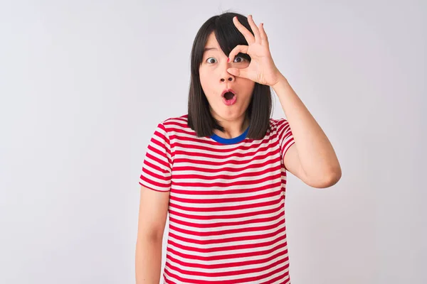 年轻漂亮的中国女人穿着红色条纹T恤在孤立的白色背景做Ok手势震惊惊讶的脸 眼睛透过手指看 不信的表达 — 图库照片