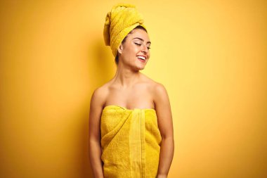 Genç güzel kadın havlu giyen izole sarı arka plan üzerinde yüz üzerinde gülümseme ile yan bakarak, doğal ifade duş sonra. Güven gülüyor.
