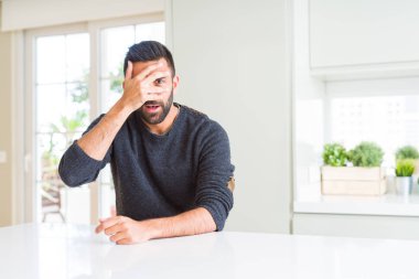 Yakışıklı İspanyol adam evde rahat kazak giyiyor şok kapsayan yüz ve gözler ile el, utanmış ifade ile parmaklar bakarak.