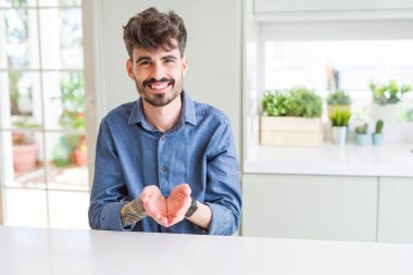 Beyaz masada oturan rahat gömlek giyen genç adam el avuç içi birlikte alma veya jest vererek gülümsüyor. Tutma ve koruma
