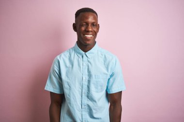 Seksi ifade, neşeli ve mutlu yüz ile kamera bakarak izole pembe arka plan üzerinde ayakta mavi rahat gömlek dikilen Afrikalı Amerikalı adam.