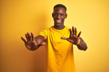 Genç Afrikalı Amerikalı adam el avuç içi, öfkeli ve hayal kırıklığı ifade ile durdurma jest yapıyor izole sarı arka plan üzerinde ayakta rahat t-shirt giymiş