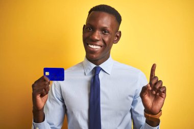 African Amerikan işadamı tutan kredi kartı ayakta izole sarı arka plan çok mutlu ile işaret el ve parmak yan