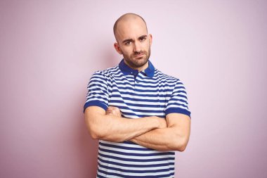 Sakal ile genç kel adam rahat çizgili mavi t-shirt üzerinde pembe izole arka plan şüpheci ve sinir, kesişmiş kolları ile yüz üzerinde ifade onaylamıyor. Negatif kişi.