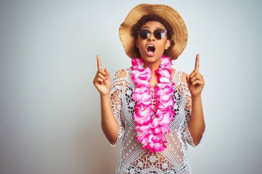 Afro saç ile genç Afrikalı Amerikan kadın izole arka plan üzerinde çiçek Hawaii Lei giyiyor şaşırdı ve görünümlü ve parmaklar ve yükseltilmiş kollar ile işaret şaşırttı.