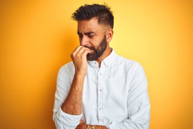 Hint işadamı izole sarı arka plan üzerinde ayakta beyaz zarif gömlek giyiyor vurguladı ve ağız ısırma tırnakları ile gergin bakıyor. Anksiyete sorunu.