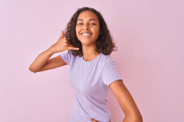 Genç Brezilyalı kadın, telefonda konuşmak gibi el ve parmaklar ile telefon jest yaparken gülümseyen izole pembe arka plan üzerinde ayakta t-shirt giyiyor. İletişim kavramları.