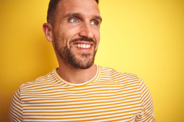 Yakın sarı izole arka plan üzerinde rahat t-shirt giyen genç yakışıklı adam yüz, doğal ifade gülümseme ile yan bakıyor. Gülmekten emin.