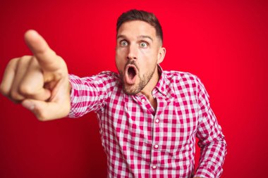 Kırmızı izole arka planda genç yakışıklı adam parmak ile Işaret ileriye sürpriz, açık ağız hayran ifadesi, ön bir şey