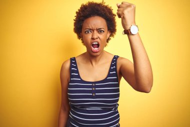 Beauitul Afrika Amerikan kadın izole sarı arka plan üzerinde yaz t-shirt giyen öfkeli ve deli öfke ile bağırırken yumruk sinirli ve öfkeli yetiştirmek. Öfke ve agresif kavram.