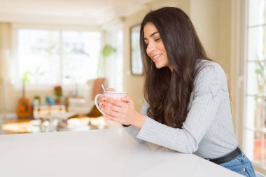 Güzel genç kız evde bir fincan kahve içme ve gülümseyen