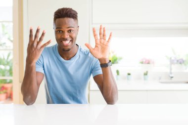 Yakışıklı afro-amerikan adam evde gösteren rahat t-shirt giyen ve parmakları ile işaret ederken emin ve mutlu gülümsüyor.