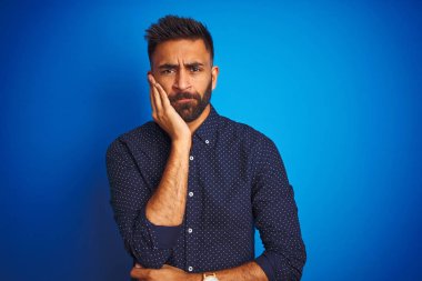 Genç hint zarif adam izole mavi arka plan üzerinde duran gömlek giyen yorgun görünümlü ve çapraz kolları ile depresyon sorunları ile sıkılmış düşünme.