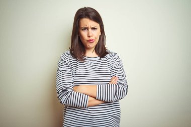 Beyaz izole arka plan üzerinde çizgili kazak giyen genç güzel esmer kadın şüpheci ve sinir, Çapraz kollar ile yüz üzerinde ifade onaylamıyor. Negatif kişi.