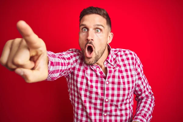 Kırmızı izole arka planda genç yakışıklı adam parmak ile Işaret ileriye sürpriz, açık ağız hayran ifadesi, ön bir şey
