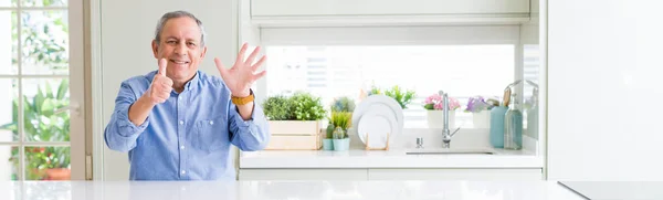 Wide angle perspective of handsome senior man at home showing and pointing up with fingers number six while smiling confident and happy.