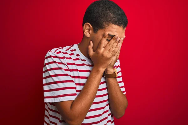 年轻的英俊阿拉伯男子穿着条纹T恤在孤立的红色背景与悲伤的表情覆盖脸与双手 而哭泣 抑郁症概念 — 图库照片