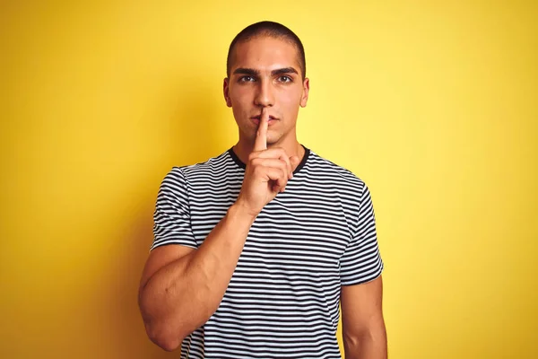 年轻的英俊男子穿着条纹T恤在黄色孤立的背景要求安静与手指在嘴唇上 沉默和秘密概念 — 图库照片