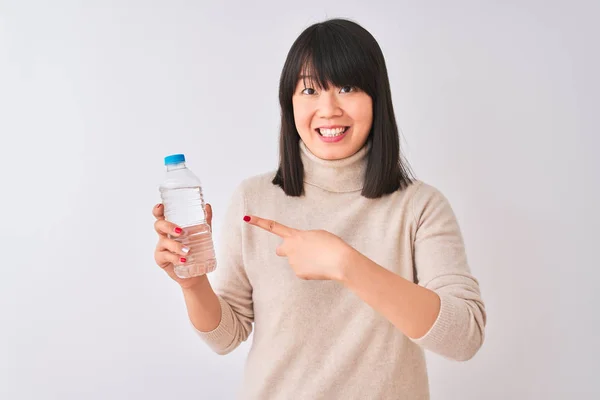 年轻美丽的中国女人拿着一瓶水在孤立的白色背景很高兴指着手和手指 — 图库照片