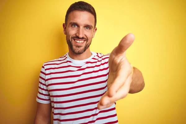 年轻的帅哥穿着休闲的红色条纹T恤 在黄色孤立的背景微笑友好地表示握手作为问候和欢迎 成功的业务 — 图库照片