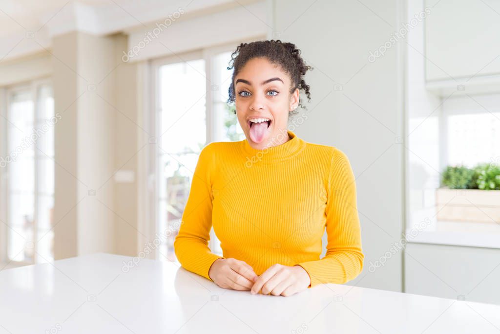 Beautiful african american woman with afro hair wearing a casual yellow sweater sticking tongue out happy with funny expression. Emotion concept.