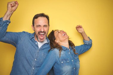 Güzel orta yaş çift birlikte izole sarı arka plan üzerinde ayakta Dans mutlu ve neşeli, hareketli rahat ve kendinden emin müzik dinleme