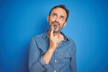 İzole mavi arka plan üzerinde gri saçlı yakışıklı Orta Çağ kıdemli adam çene üzerinde parmak ile şüphe hakkında konsantre düşünme ve merak bakıyor