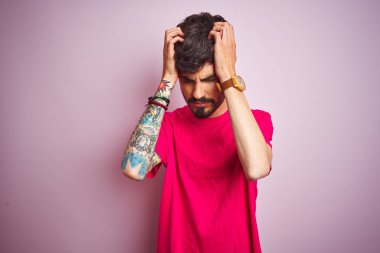 Dövmeli genç adam izole pembe arka plan üzerinde ayakta t-shirt giyen baş ağrısı umutsuz muzdarip ve stresli çünkü ağrı ve migren. Eller baş üstünde.