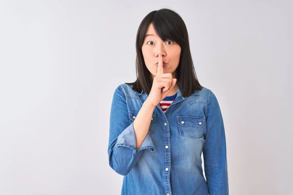 年轻美丽的中国妇女穿着牛仔衬衫在孤立的白色背景要求安静与手指在嘴唇上 沉默和秘密概念 — 图库照片