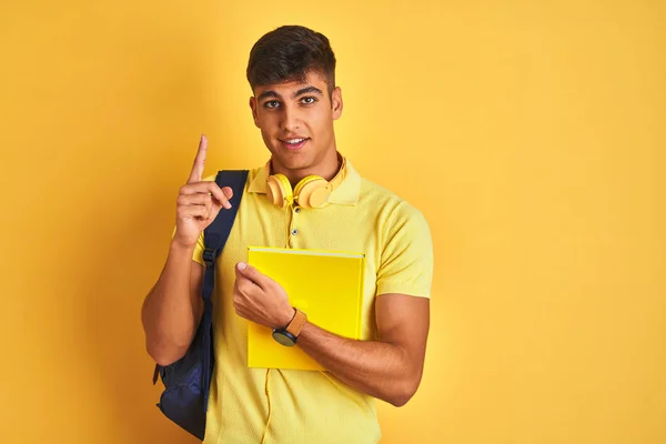 印度学生男子穿着背包耳机笔记本在孤立的黄色背景惊讶与想法或问题指向手指与快乐的脸 — 图库照片