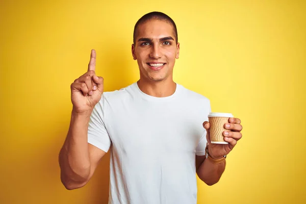 黄色の孤立した背景の上にコーヒーを持ち去るグラスを飲む若いハンサムな男は 幸せな顔で指を指すアイデアや質問に驚きました ナンバーワン — ストック写真