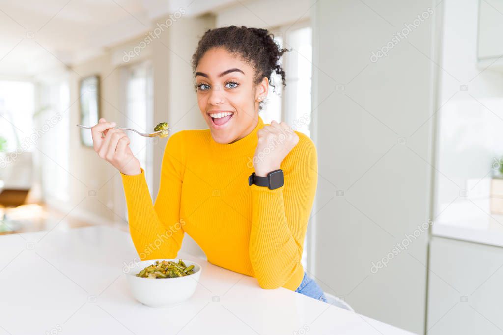 Young african american woman eating healthy green vegatables screaming proud and celebrating victory and success very excited, cheering emotion