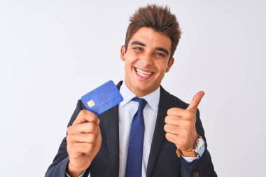 Genç yakışıklı işadamı takım elbise giyen izole beyaz arka plan üzerinde büyük bir gülümseme ok işareti yapıyor mutlu kredi kartı tutan, parmakları ile başparmak, mükemmel işareti