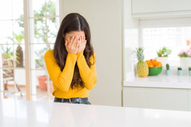 Ağlarken elleri ile yüz kapsayan üzücü ifade ile beyaz masada evde genç güzel kadın. Depresyon konsepti.