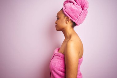 Afrika Amerikan kadın banyo sonra duş havlu giyen pembe izole arka planda yan arıyor, rahat bir gülümseme ile doğal yüz ile profil poz rahatlayın.