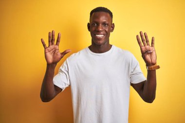 Beyaz t-shirt izole sarı arka plan üzerinde ayakta giyen genç Afrikalı Amerikalı adam gösteren ve parmak numarası dokuz ile işaret kadar güven ve mutlu gülümseyen.