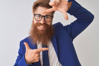 Genç kızıl İrlandalı işadamı takım elbise ve gözlük giyerek izole beyaz arka plan üzerinde mutlu yüz ile elleri ve parmakları ile çerçeve yapma gülümseyerek. Yaratıcılık ve fotoğrafçılık konsepti.