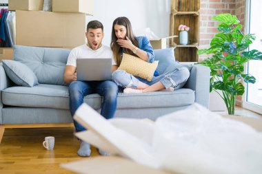 Genç güzel çift yeni evin kanepede oturan rahatlatıcı bir sürpriz yüz ile şok korkuyor bilgisayar laptop kullanarak, korkuyor ve korku ifadesi ile heyecanlı