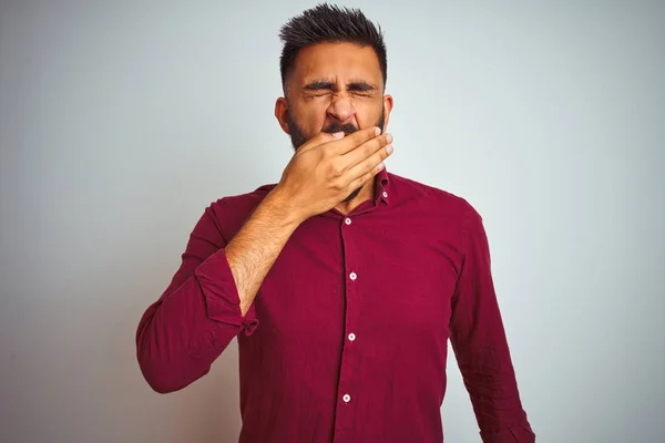 Young indian man wearing red elegant shirt standing over isolated grey background bored yawning tired covering mouth with hand. Restless and sleepiness.