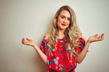 Genç güzel kadın beyaz izole arka plan üzerinde çiçek t-shirt giyen habersiz ve kollar ve eller kaldırdı ile karışık ifade. Şüphe kavramı.