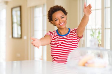 Genç güzel afro-amerikan kadın evde sarılmak için açık kollarla gülümseyerek kameraya bakarak. Mutluluğu kucaklayan neşeli ifade.